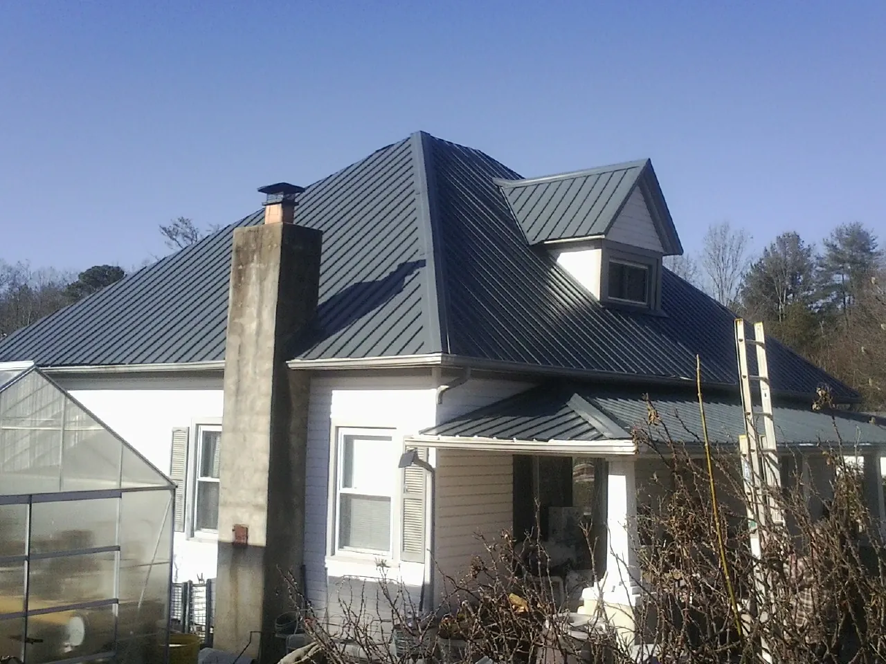 Dark blue standing seam metal roof on a white farmhouse with dormer — Slate & Tile Roof Repair by Roofing Brothers in Riverside